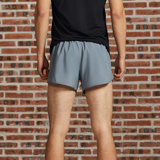 Man wearing grey athletic shorts and black t-shirt standing against brick wall from behind