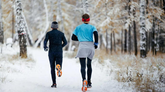 Two runners jogging on a snowy forest trail in winter running gear